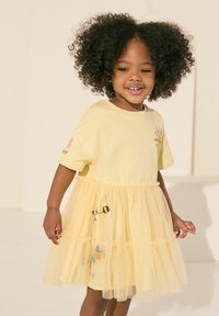 Robe en coton jaune avec des manches courtes, jupe en tulle et motifs floraux et abeilles brodés. Présente un tissu doux et texturé.