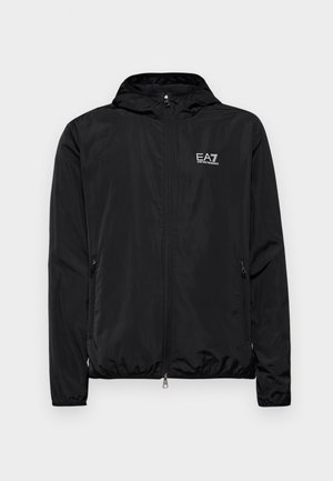 Casaco leve preto com capuz, frente com fecho éclair, dois bolsos laterais e logotipo EA7 branco no peito. Tecido suave e brilhante.