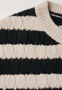 Strickpullover mit abwechselnden Streifen aus flauschigem schwarzem und cremefarbenem Material, einem gerippten Rundhalsausschnitt und erhabenen, kreisförmigen Mustern.