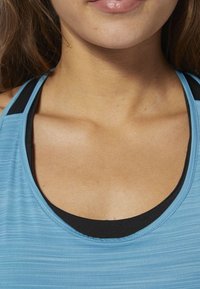 Light blue athletic tank top with a scoop neckline, layered over a black sports bra. Material appears smooth with subtle texture.