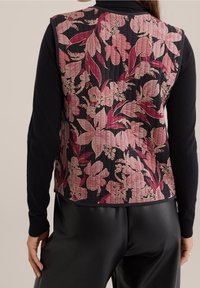 Blommig väst i svart tyg med mönster av rosa och vinröda blommor, quiltad textur och en åtsittande silhuett. Svarta ärmar sträcker sig från basen.