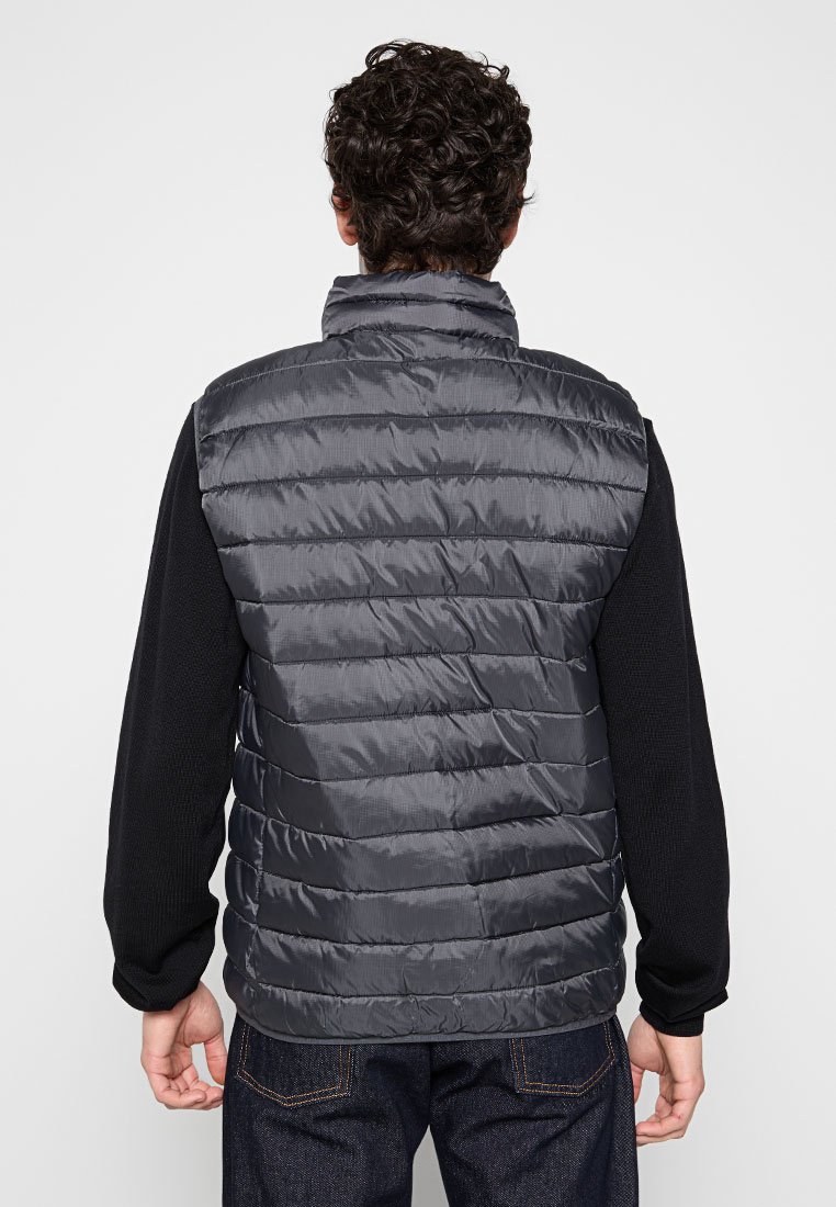 Gilet imbottito grigio scuro con colletto alto, caratterizzato da una texture trapuntata e una finitura liscia e lucida. Abbinato a una maglietta nera a maniche lunghe.