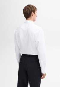 Weißes Langarmhemd mit button-down Kragen, kombiniert mit dunklen Hosen. Das Hemd zeichnet sich durch eine glatte Textur und eine taillierte Passform aus.