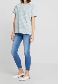 Niebieska kraciasta bluzka z krótkim rękawem, zestawiona z jasnoniebieskimi obcisłymi dżinsami i białymi balerinami. Koszula ma okrągły dekolt i luźny krój.