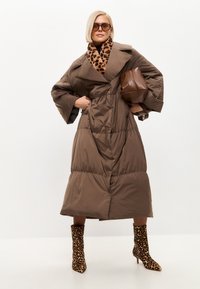 Brun polstret frakke med stor krave, taljeret talje og brede ærmer. Kombineret med leopardmønstret tørklæde og matchende ankelstøvler.