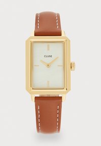 Montre rectangulaire dorée avec un cadran vert pâle texturé, des indicateurs d'heure minimalistes et un bracelet en cuir brun avec des coutures blanches.
