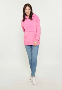 Felpa con cappuccio rosa con design a pannelli testurizzati, tasca a marsupio e polsini a costine, abbinata a jeans skinny blu chiaro e sneakers bianche.