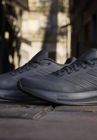 Pair of dark running shoes with Cloudfoam soles placed on cobblestone street in outdoor urban setting.