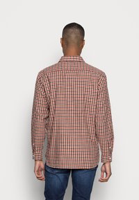 Camicia a quadri rossa e beige con colletto classico, maniche lunghe e polsini con bottoni, realizzata in tessuto morbido, vista da dietro.