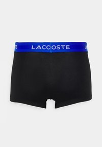 Shorts de boxer noirs en matériau doux avec une ceinture élastique bleue arborant le logo « Lacoste ». L'arrière présente un petit détail d'aération.
