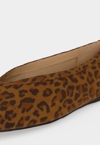 Chaussure plate marron avec motif léopard noir et doublure intérieure beige, inclinée pour montrer la vue latérale et partielle de dessus.