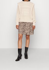 Chunky krämfärgad stickad tröja med texturerat mönster, i kombination med en knälång beige kjol med ett svart abstrakt tryck och svarta klackkängor.