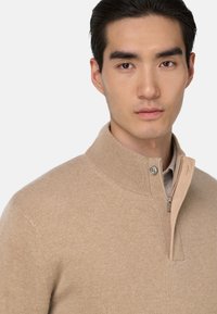 Beige, knitted sweater with a high collar and zip closure. Features a smooth texture and ribbed cuffs. Minimalist design with subtle detailing.