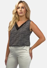 Czarna i biała top bez rękawów w wzory z dekoltem w kształcie V i koronkowym wykończeniem, połączony z jasnobeżowymi spodniami o dopasowanym kroju.