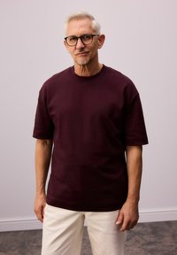Mørkerød kortærmet T-shirt i en afslappet pasform, lavet af blødt stof. Har en rund halsudskæring og en glat, jævn tekstur.