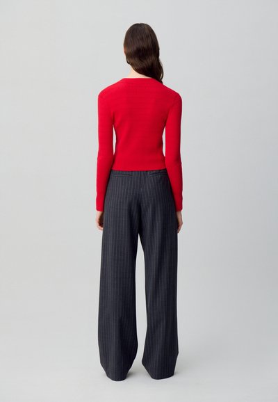 Top a maniche lunghe rosso a coste abbinato a pantaloni a vita alta larghi grigi scuri a righe sottili. Design semplice, texture liscia.