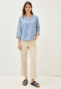 Blouse en coton rayée bleue avec un léger motif de feuilles, manches trois-quarts, associée à un pantalon large beige et des sandales sombres.