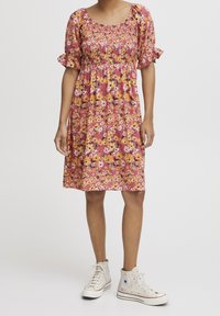 Kwiatowa sukienka w kolorze różowym z krótkimi bufkami, gorsetem marszczonym i warstwową spódnicą. Połączona z szarymi sneakersami typu high-top.