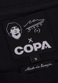 Zwarte stoffen label met een witte grafiek van een persoon, de tekst "DIEGO", "x COPA", maat "S" en de tekst "Gemaakt in Europa".
