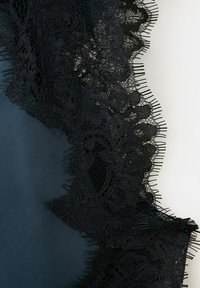 Bordure en dentelle florale noire à bords festonnés superposée à un tissu foncé, montrant des détails fins de fil et des motifs complexes en maille.