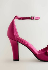 Scarpa alta in satin rosa con cinturino e fibbia, caratterizzata da un dettaglio a fumetto sulla parte anteriore e una finitura texturizzata sul tacco.