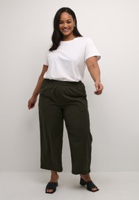 T-shirt blanc à manches courtes accompagné de pantalons cropped à taille élastique vert olive et de sandales à glissière noires, offrant une coupe décontractée.