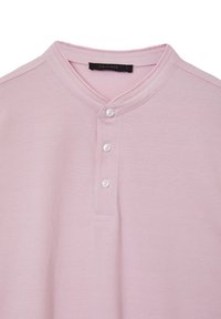 Polo shirt rosa chiaro con colletto button-down, realizzato in tessuto testurizzato, con tre bottoni e un'etichetta che riporta la scritta "CALLIOPE".