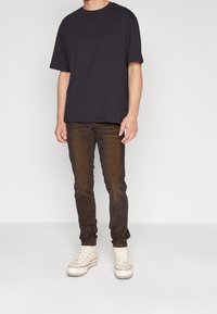 Černé tričko s krátkým rukávem, které je spárováno se slim-fit tmavě hnědými džíny a bílými vysokými teniskami. Jednoduchý design, bavlněný materiál.