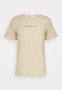 Béžové bavlněné tričko s krátkým rukávem a kulatým výstřihem. Na přední straně se nachází hnědý potisk loga "Calvin Klein Jeans".