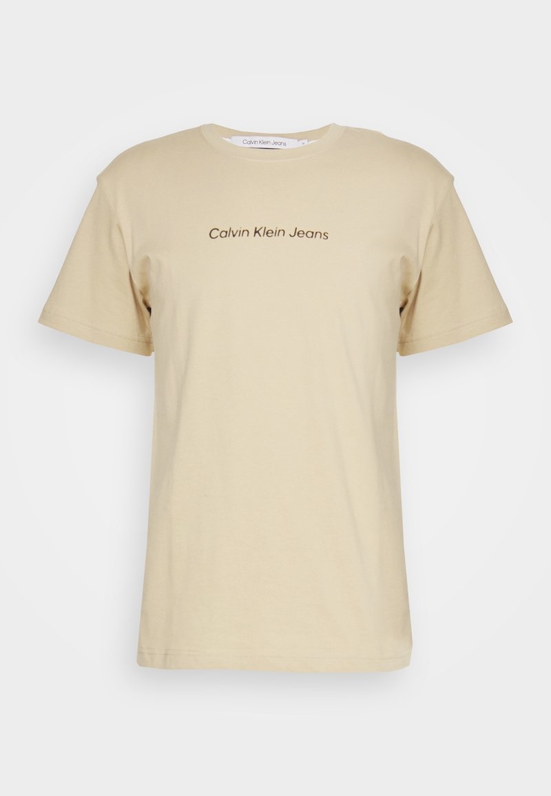 Béžové bavlněné tričko s krátkým rukávem a kulatým výstřihem. Na přední straně se nachází hnědý potisk loga "Calvin Klein Jeans".