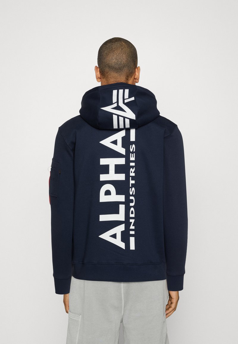 Hanorac bleumarin cu glugă, având un mare logo alb "ALPHA INDUSTRIES" pe spate, cu șnur pentru glugă și manșete și tiv ribbed.