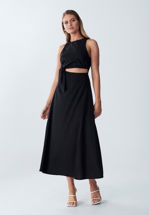 Black two-piece dress featuring a fitted crop top with a tie detail at the waist and a flowing, ankle-length skirt. Smooth fabric texture.