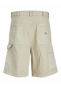 Béžové cargo šortky s několika velkými kapsami a poutky na opasek, které mají na pravé zadní kapse malou obdélníkovou značkovou nálepku.