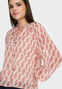 Blouse légère rose avec imprimé paisley, col à volants, manches longues, devant à boutons et texture subtile.