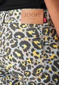 Leopardi mustriga denimeed, millel on sinised, kollased ja mustad mustrid; heledast nahast silt "JOOP! JEANS" vöökohtadel.