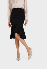 Gonna nera a ruota con orlo arricciato, abbinata a scarpe slingback beige con motivo, con punta affusolata e dettagli decorativi in metallo.