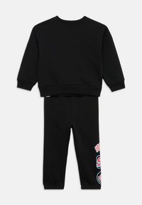 Fekete pulóver hosszú ujjakkal és bordázott mandzsettákkal, hozzáillő melegítőnadrággal, melyen színes nyomott díszítések találhatók a lábszáron.