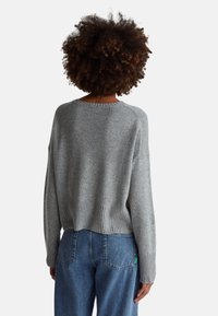 Szary sweter dziany o luźnym kroju, z prążkowanym dołem i mankietami oraz opuszczonymi ramionami, zestawiony z wysokim stanem niebieskich dżinsów.