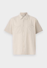 Camisa de botones de manga corta en beige claro con una tela texturizada, dos bolsillos en el pecho y un cuello puntiagudo.