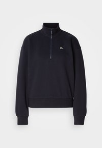 Navy blue sweatshirt with a high collar and quarter-zip, featuring long sleeves and a ribbed hem. Includes a small green logo on the chest.