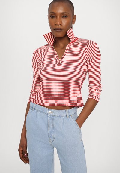 Haut à manches longues rayé rouge et blanc avec un col montant et une coupe cropped. Associé à un jean taille haute bleu clair.