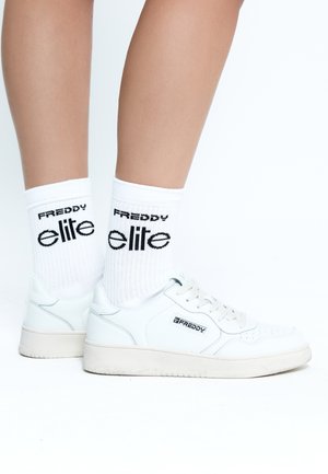 Sneakers bianche in pelle testurizzata, con dettagli perforati e suole chiare. Abbinati a calzini bianchi a coste con marchio nero.