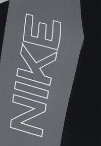 Tissu gris et noir avec le logo "NIKE" en blanc bordé, imprimé verticalement sur la section grise, montrant une couture détaillée le long des bords.