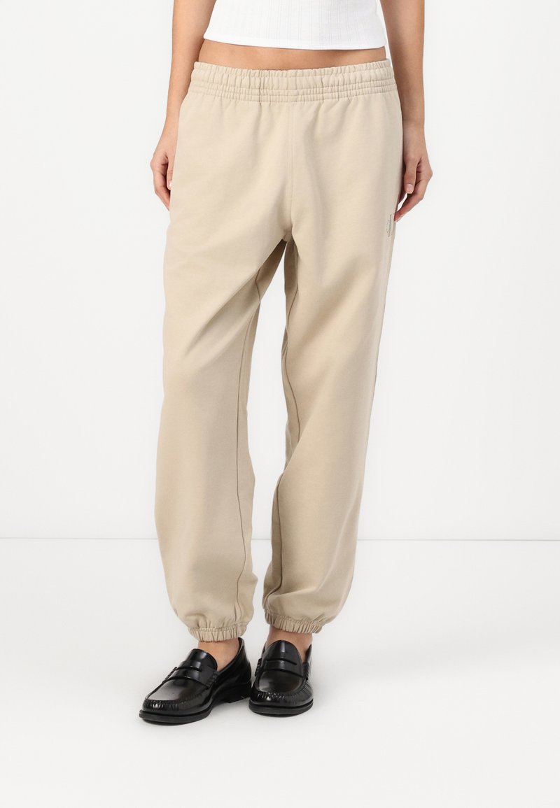 Calças jogger bege com cós elástico e punhos de tornozelo ajustados. Feitas de material suave, com detalhes de costura discretos.