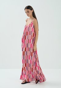 Długa, bezrękawna sukienka z kolorowym wzorem składającym się z różowych, czerwonych i fioletowych pionowych pasków. Zwiewny materiał o luźnym kroju.
