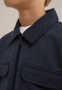 Giacca a zip color blu navy con un motivo testurizzato, dotata di colletto a punta e due tasche sul petto. Zip nera con tirazip di marca.