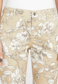 Beige Blumendruckhose mit weißen und silbernen Mustern. Mit einem Knopfverschluss vorne und Taschen, aus leichtem Stoff gefertigt.