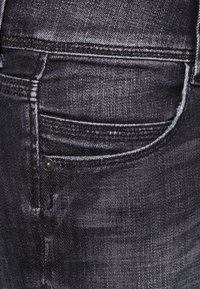 Jeans de denim oscuro con un diseño clásico de cinco bolsillos, un leve desvanecimiento y costuras en contraste, además de un pequeño remache metálico en el bolsillo frontal.