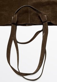 Cintura in suede marrone con cuciture bianche posata piatta su uno sfondo bianco, che mostra le cinghie sovrapposte e una cucitura.