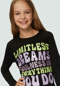 Schwarzes Langarm-T-Shirt mit auffälligem, großen Text in Grün und Lila: "Grenzenlose Träume, Coolness in allem, was du tust."